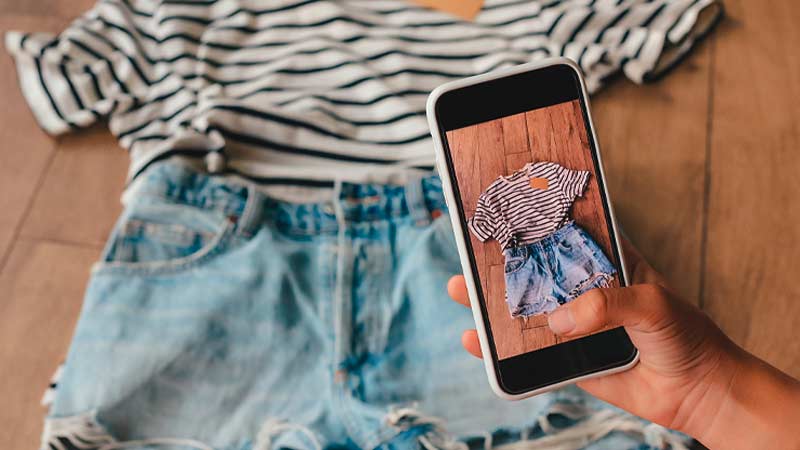 Grande plano de alguém a fotografar roupa com um telemóvel - alusão a venda online de roupa em segunda mão